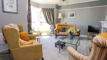 A living room with a sofa, armchair, and a coffee table. There is a television and a lamp.
