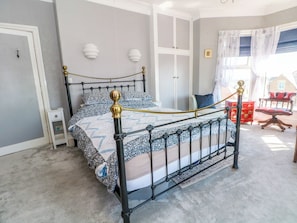 Un dormitorio con cama, mesita de noche, armario, silla y ventana con cortinas.