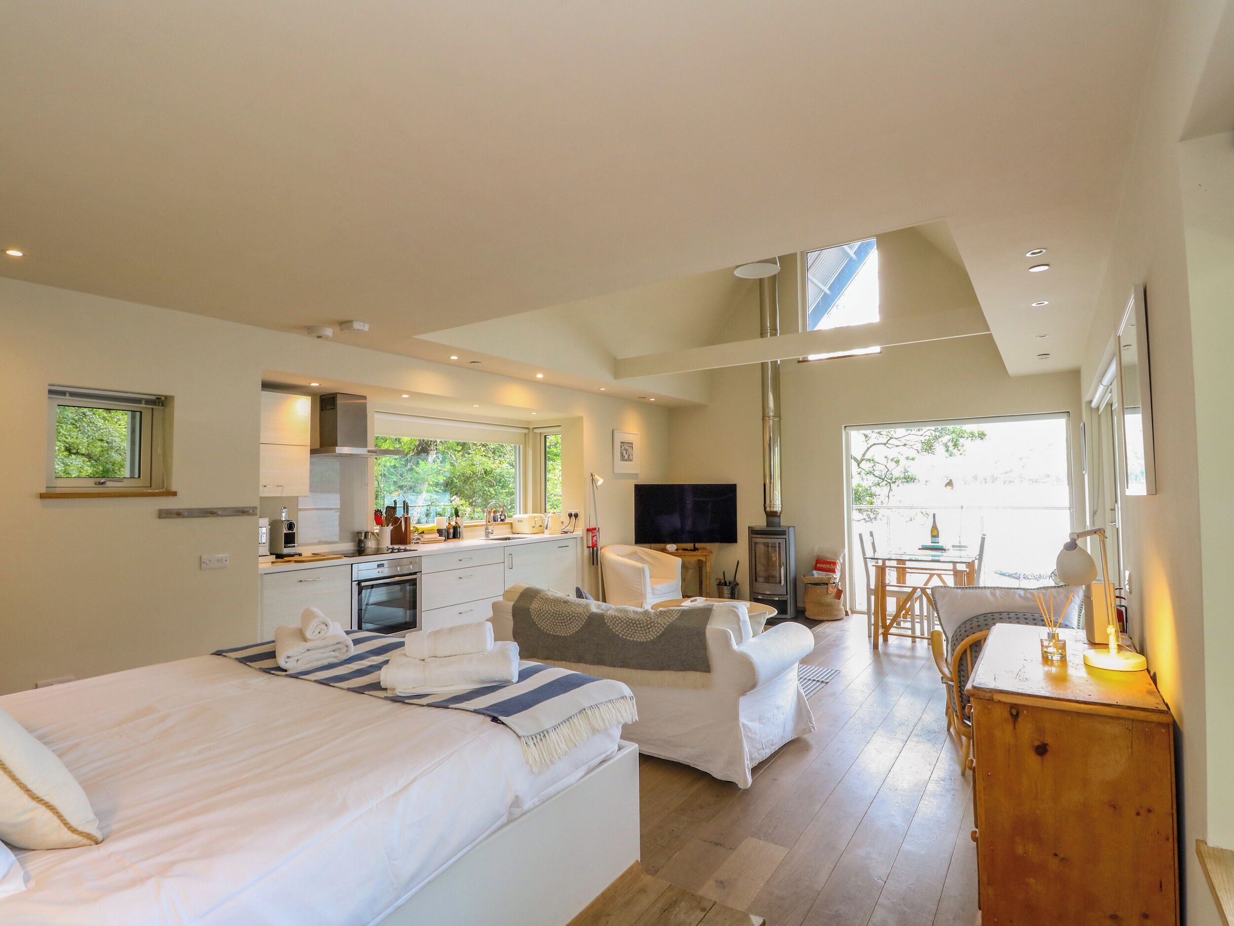 A modern hotel room with a bed, a sofa, a dining area, a TV, and a fireplace.