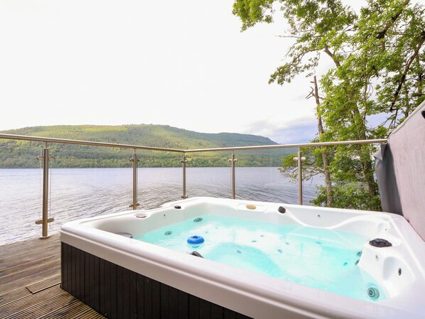A hot tub on a deck with a view of a lake and hills.