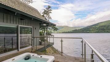 Un jacuzzi en una terraza de madera con vista a un lago y colinas.