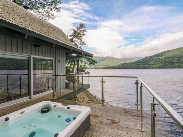 A hot tub on a wooden deck with a view of a lake and hills.
