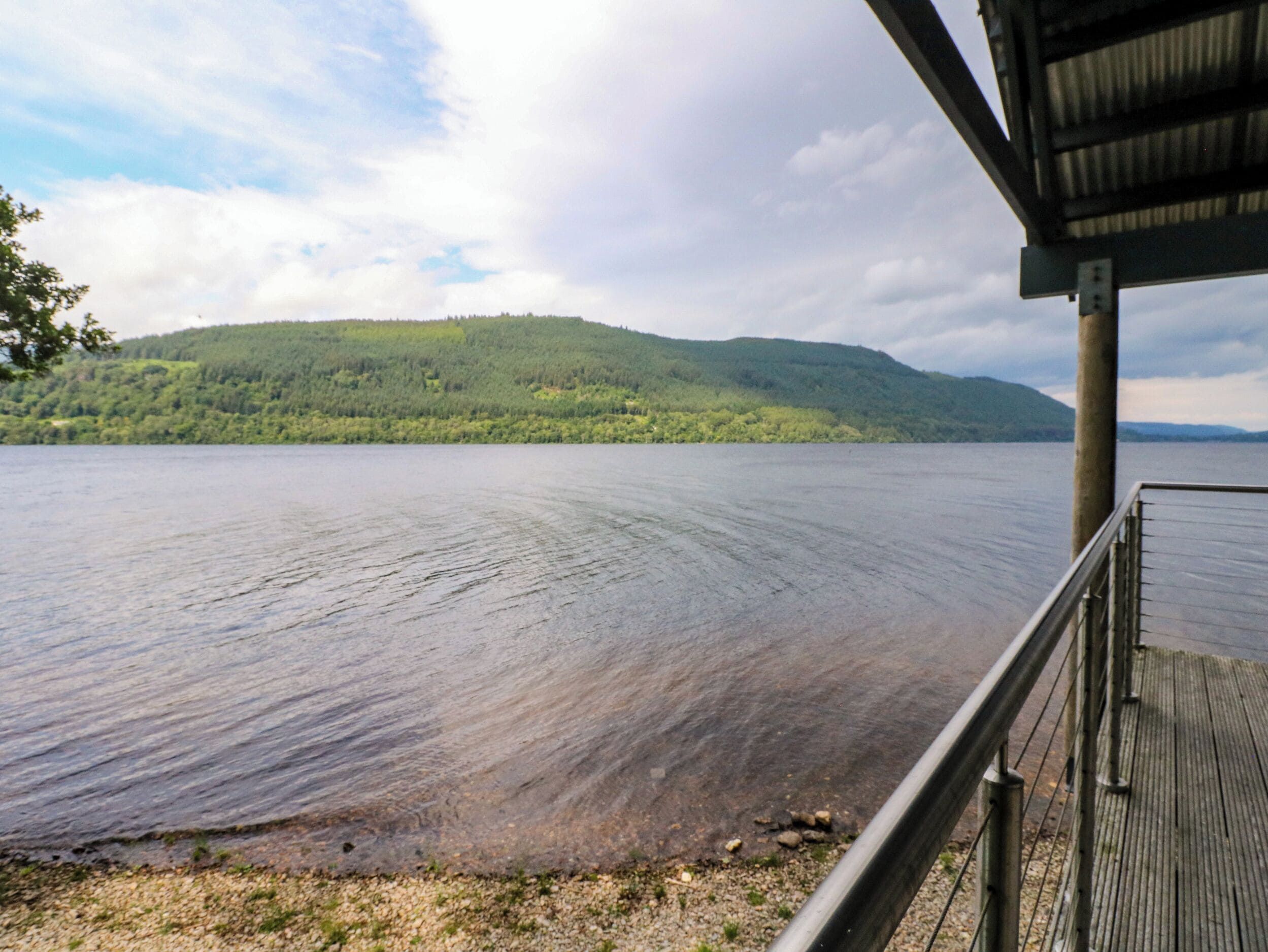 A lakeside view with a wooden deck and a metal railing.