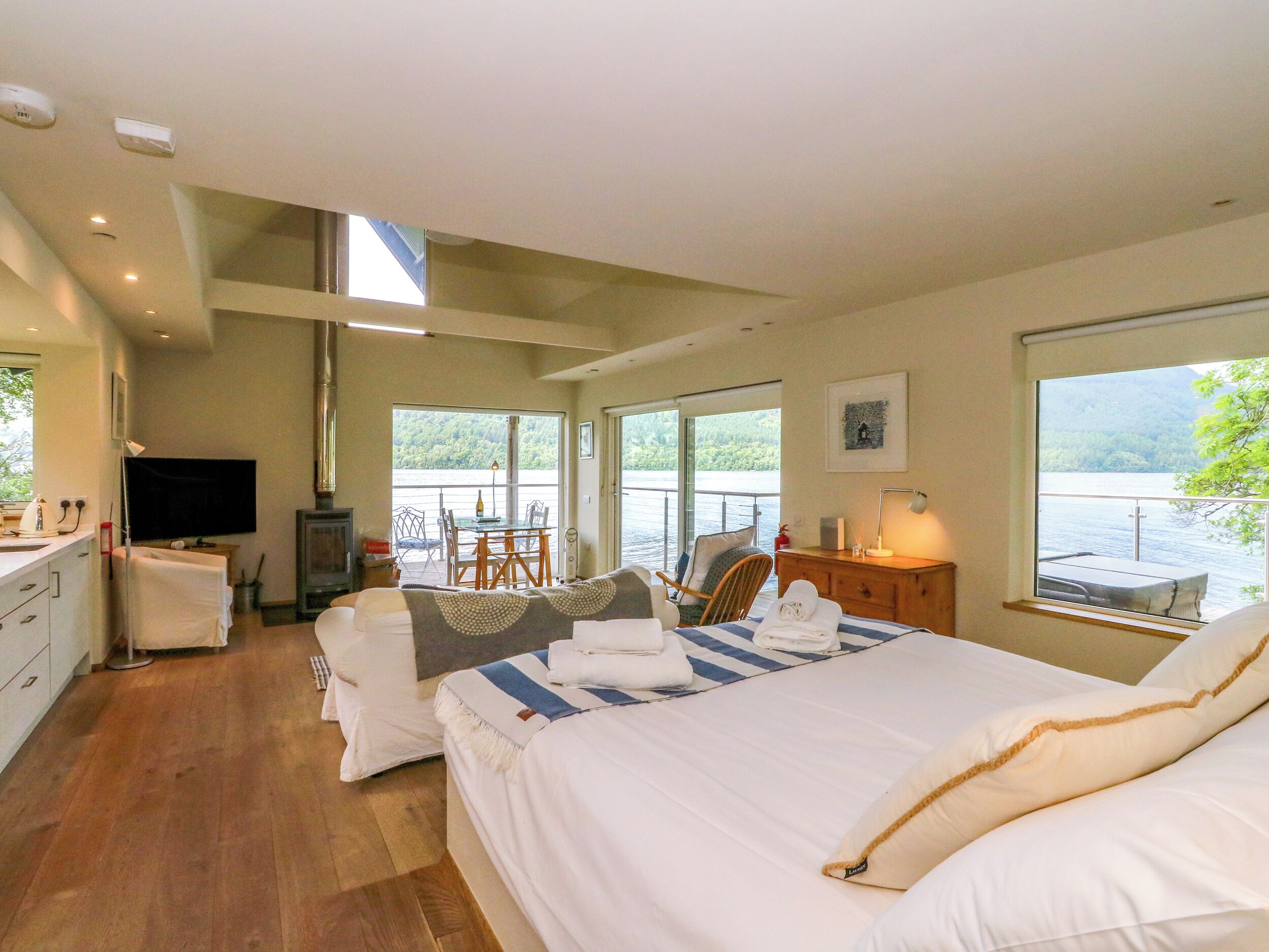 Quarto com uma cama grande, uma escrivaninha, uma cadeira, uma televisão e vista para um lago.