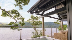 A hot tub on a deck with a view of a lake and hills.