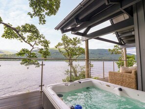 A hot tub on a deck with a view of a lake and hills. - Dipper Boathouse (Aberfeldy)