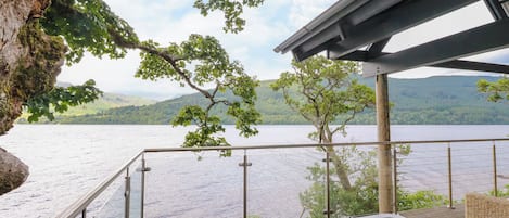 A hot tub on a wooden deck with a view of a lake and mountains.