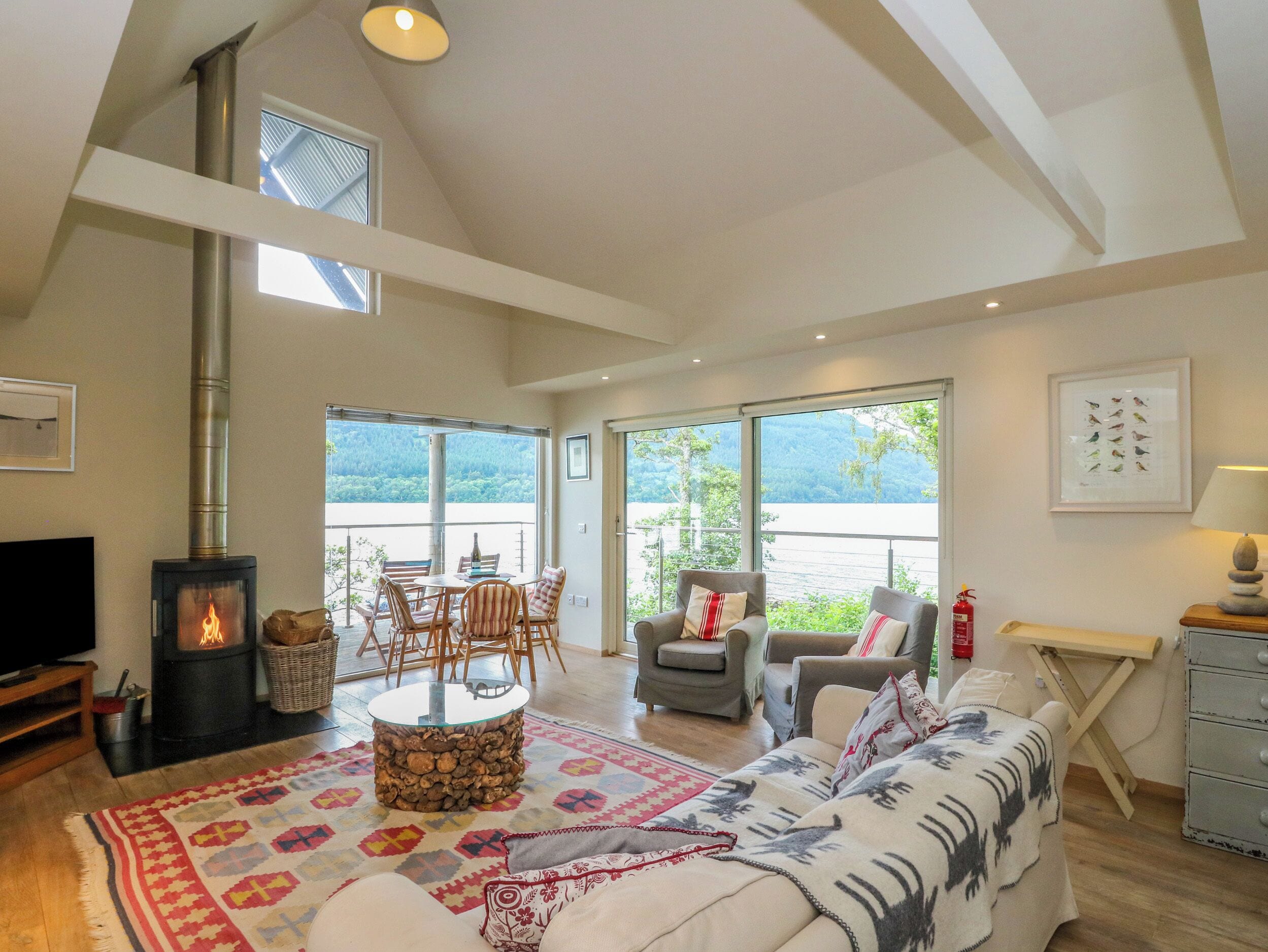 A spacious living room with a fireplace, a dining area, and large windows offering a view of the outdoors.