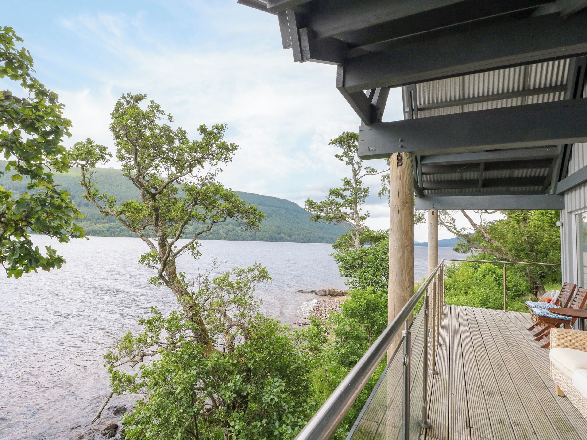Um deck de madeira com móveis de exterior com vista para um lago e colinas.