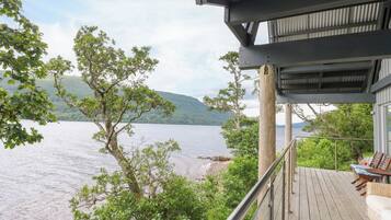 Um deck de madeira com móveis de exterior com vista para um lago e colinas.