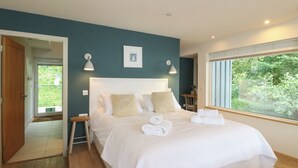 A bedroom with a bed, bedside lamps, a framed picture, and a window with a view of greenery.