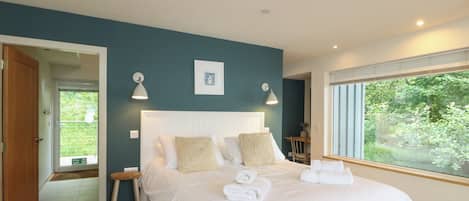 A bedroom with a bed, bedside lamps, a framed picture, and a window with a view of greenery.
