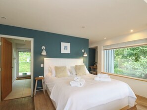 A bedroom with a bed, bedside lamps, a framed picture, and a window with a view of greenery. - Dipper Boathouse (Aberfeldy)