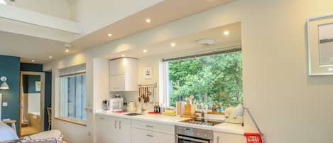 A modern kitchen with white cabinets, a built-in oven, and a window overlooking greenery.