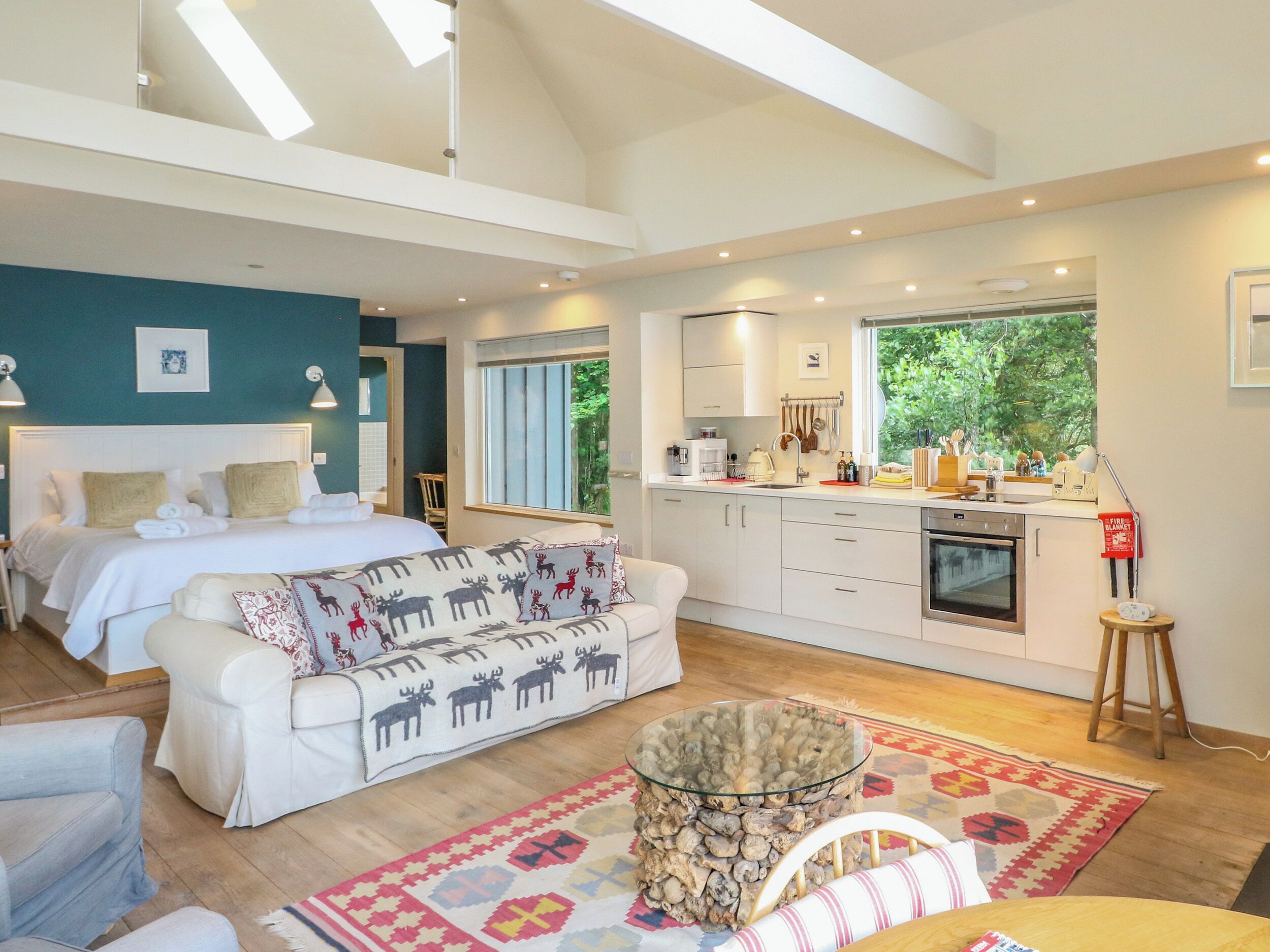 A modern bedroom with a large bed, a sofa with animal prints, a glass coffee table, and a view of the outdoors.