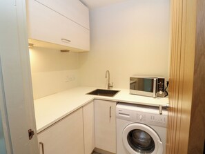 A compact kitchen with a washing machine, a microwave, and a sink. - Dipper Boathouse (Aberfeldy)