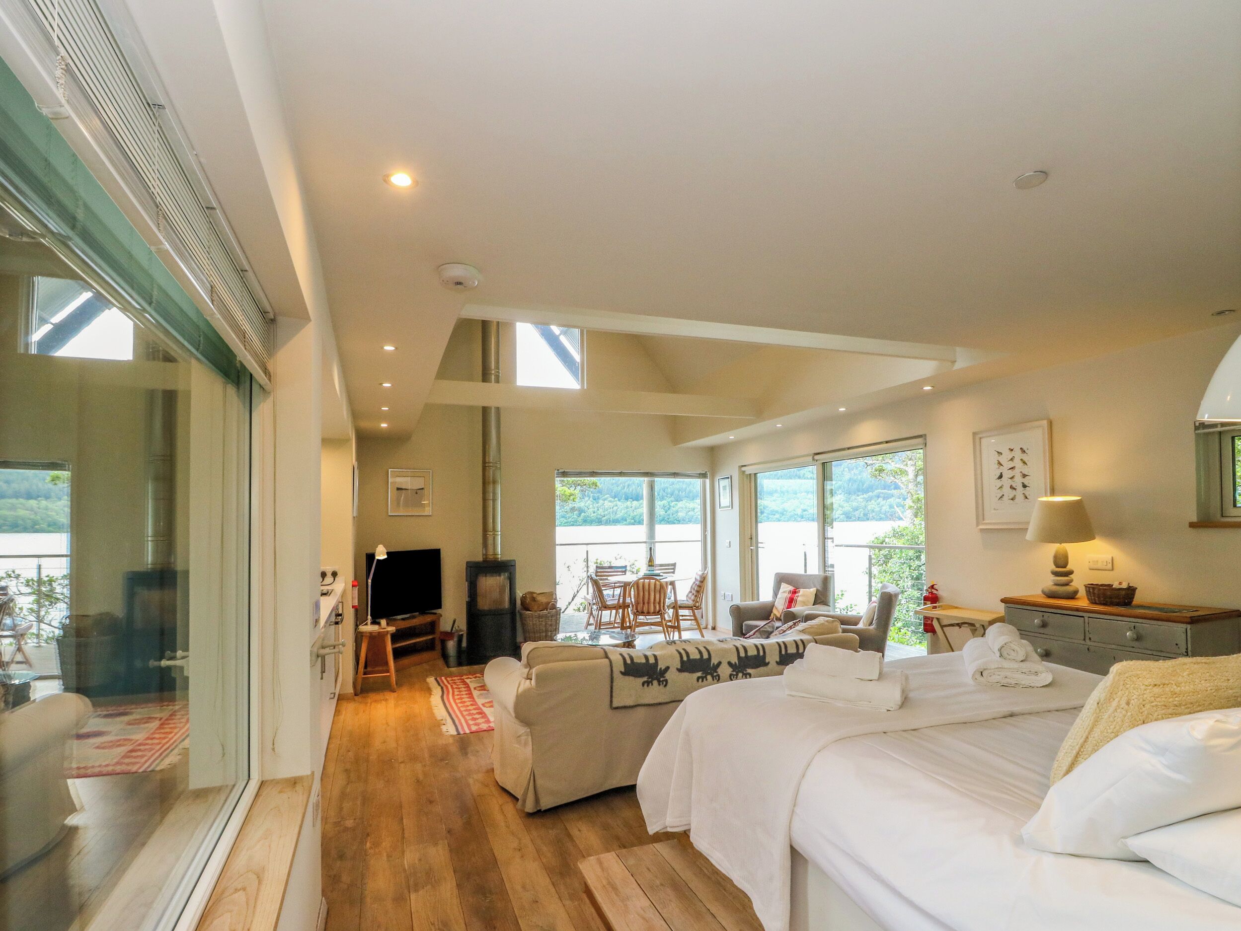 A spacious room with a large bed, a television, and a fireplace. There is a balcony with a view of the outdoors.