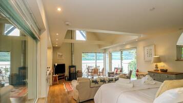 A spacious room with a large bed, a television, and a fireplace. There is a balcony with a view of the outdoors.