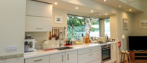 A modern kitchen with white cabinets, a built-in oven, and a window overlooking greenery.
