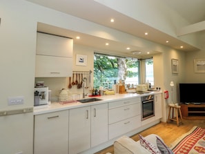 A modern kitchen with white cabinets, a built-in oven, and a window overlooking greenery.