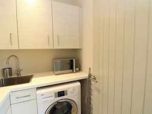 A compact kitchen with a washing machine, a microwave, and a sink. - Dipper Boathouse (Aberfeldy)