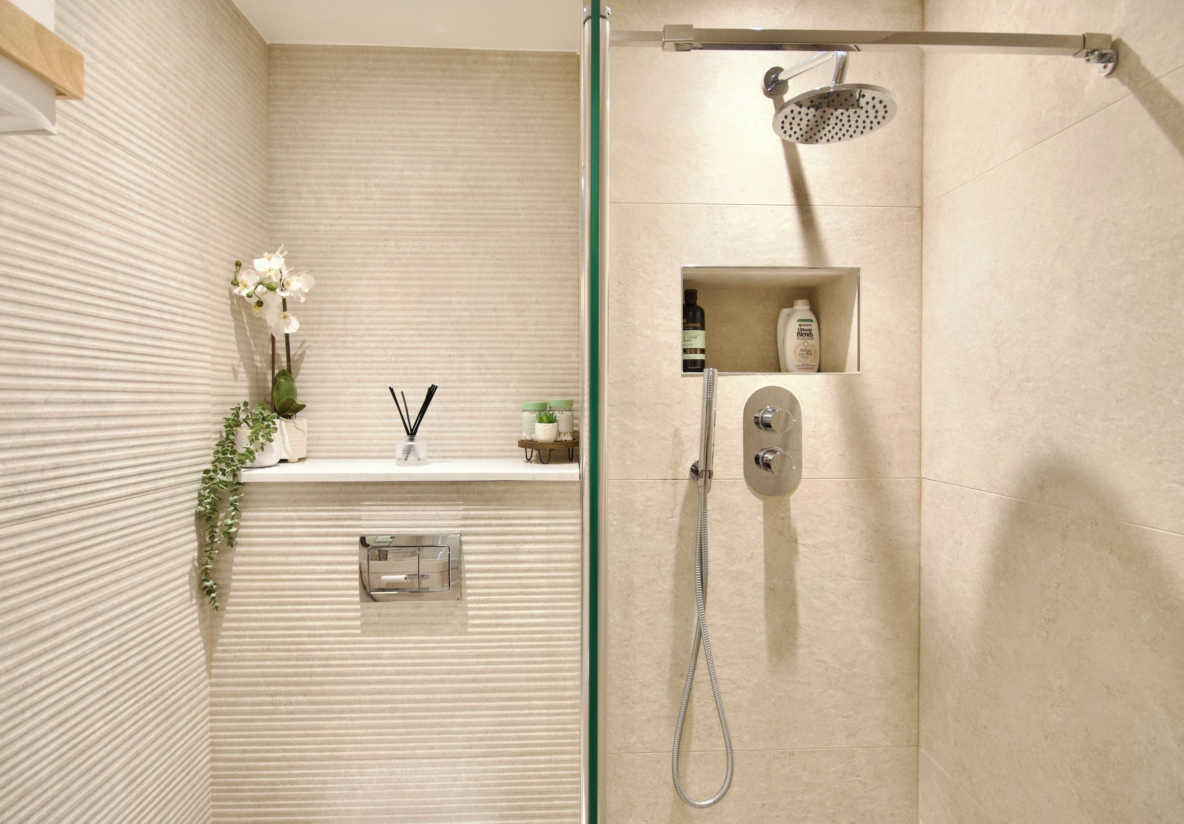 A modern bathroom with a glass shower enclosure, a built-in shelf with toiletries, and a textured wall.