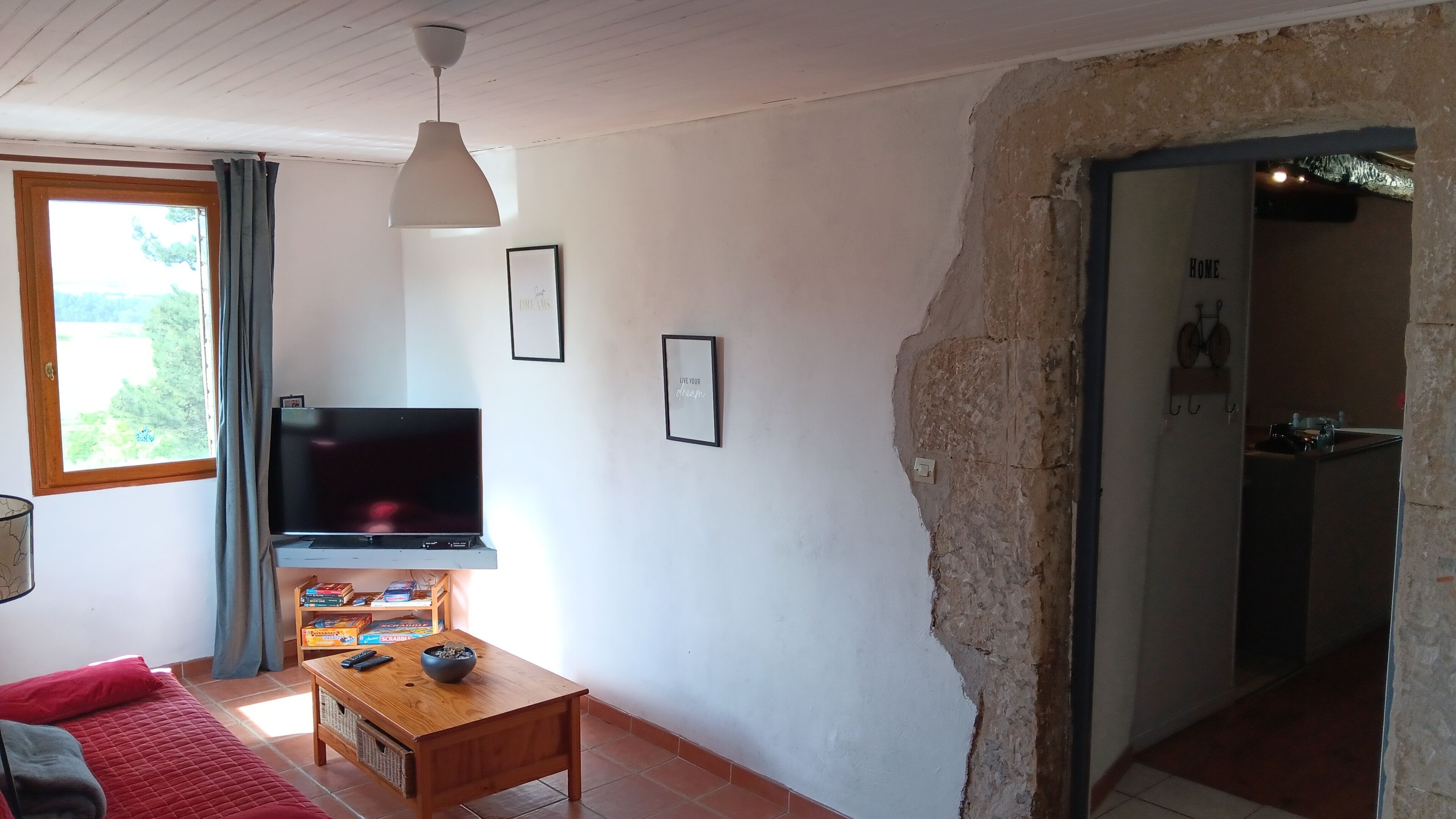 Uma sala de estar com televisão, mesa de centro de madeira e sofá vermelho.