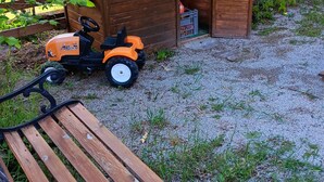 A wooden playhouse with a sign, a bench, and a toy tractor in a garden setting. - A spacious vacation rental in the countryside with a magnificent view of the Muse Valley. (Saint-Beauzély)