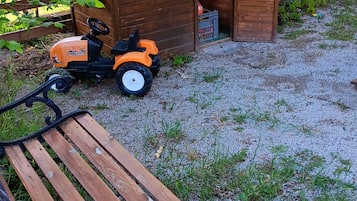 Et trælegetøjshus med skilt, bænk og en legetraktorgren i en have.