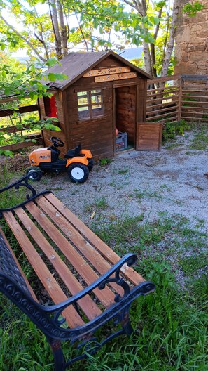 A wooden playhouse with a sign, a bench, and a toy tractor in a garden setting. - A spacious vacation rental in the countryside with a magnificent view of the Muse Valley. (Saint-Beauzély)
