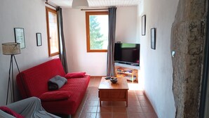 A living room with a red sofa, a wooden coffee table, a television, and a floor lamp. - A spacious vacation rental in the countryside with a magnificent view of the Muse Valley. (Saint-Beauzély)
