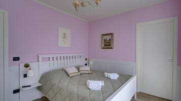 A bedroom with a bed, a nightstand, a lamp, a door, and a wall with a picture.