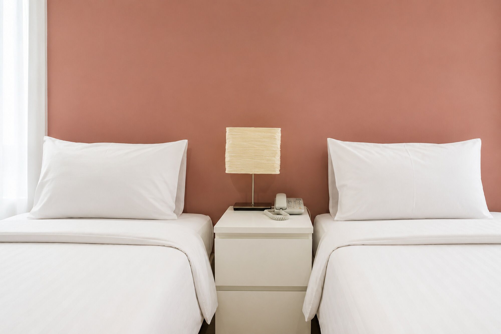 A hotel room with two beds, a nightstand, a lamp, and a telephone.
