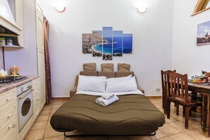 A bedroom with a bed, a dining table, a kitchen area, and a wall-mounted artwork. - PILLYHOUSE VUCCIRIA: a charming apartment at the entrance to the Vucciria Market (Palermo)