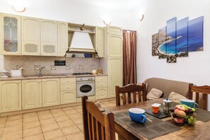 A kitchen with wooden cabinets, a dining table with chairs, a coffee maker, and a fruit bowl. - PILLYHOUSE VUCCIRIA: a charming apartment at the entrance to the Vucciria Market (Palermo)