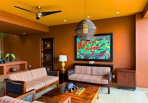 A living room with striped sofas, a coffee table, a ceiling fan, a wall-mounted painting, and a cabinet.