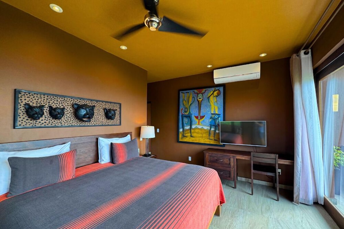 Une chambre d’hôtel équipée d’un lit, d’un bureau, d’une télévision et décorée avec des œuvres d’art aux murs.