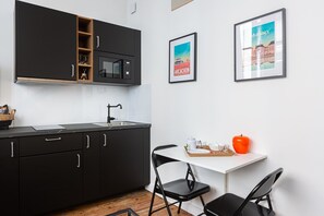 A modern kitchen with black cabinets, a microwave, and a sink. There are two framed pictures on the wall, one of a cityscape and another of a building. - Elegant AC duplex in the very heart of Bordeaux (Bordeaux)