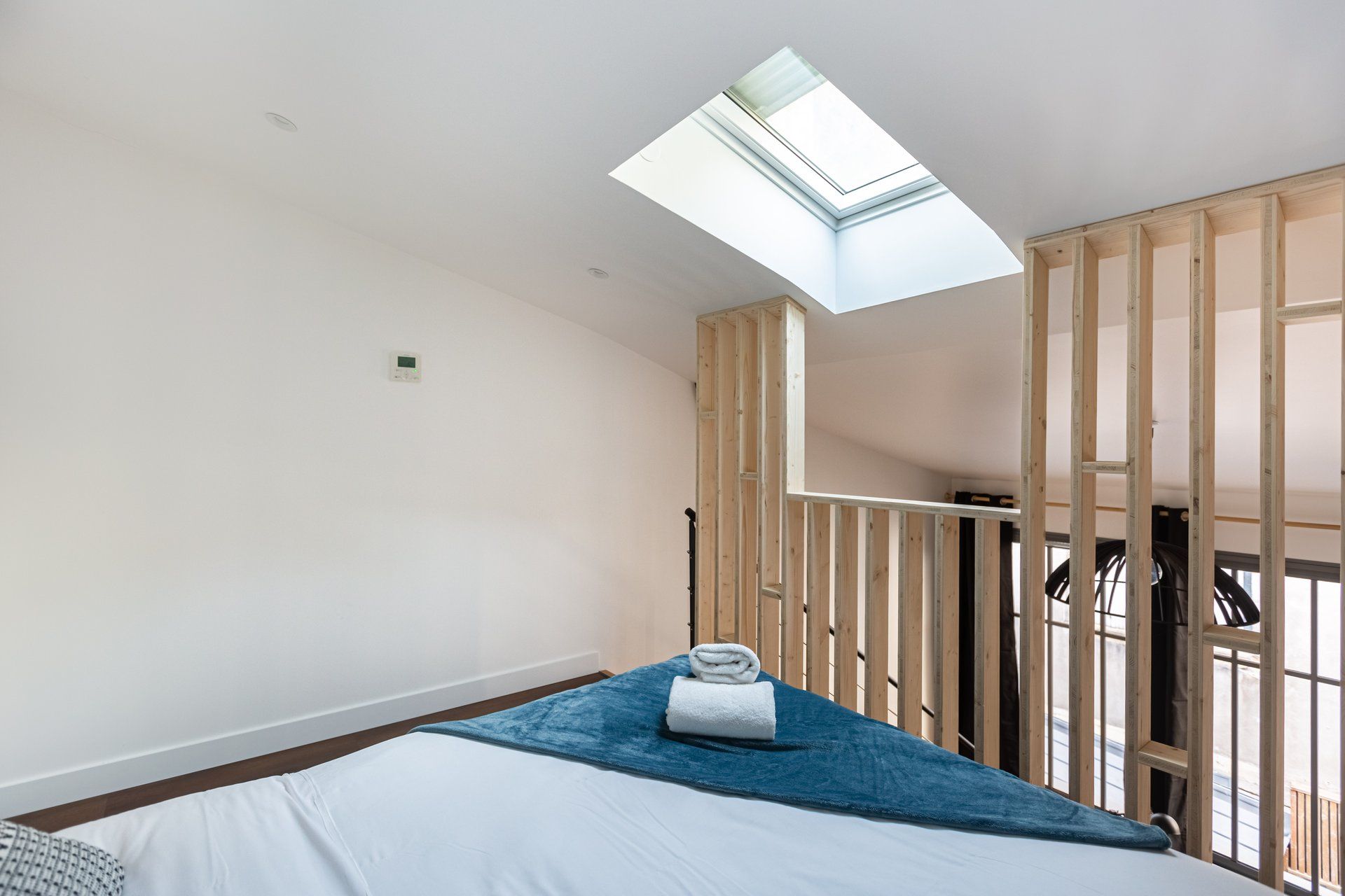 Una habitación con tragaluz, una cama con manta azul y paneles de madera.
