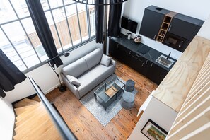 Eine moderne Wohnung mit einem grauen Sofa, einem kleinen Couchtisch, einer Küche mit schwarzen Schränken und einem großen Fenster mit Vorhängen.