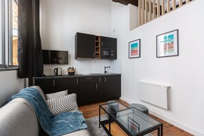 A modern kitchen with black cabinets, a microwave, and a kettle on the counter. There is a sofa with a blanket and pillows, a glass coffee table, and a radiator on the wall. - Elegant AC duplex in the very heart of Bordeaux (Bordeaux)