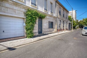 A street view with a building featuring a garage door, a window with a metal grille, and a tree growing on the wall. - Exceptional House with Private Pool Bordeaux (Bordeaux)