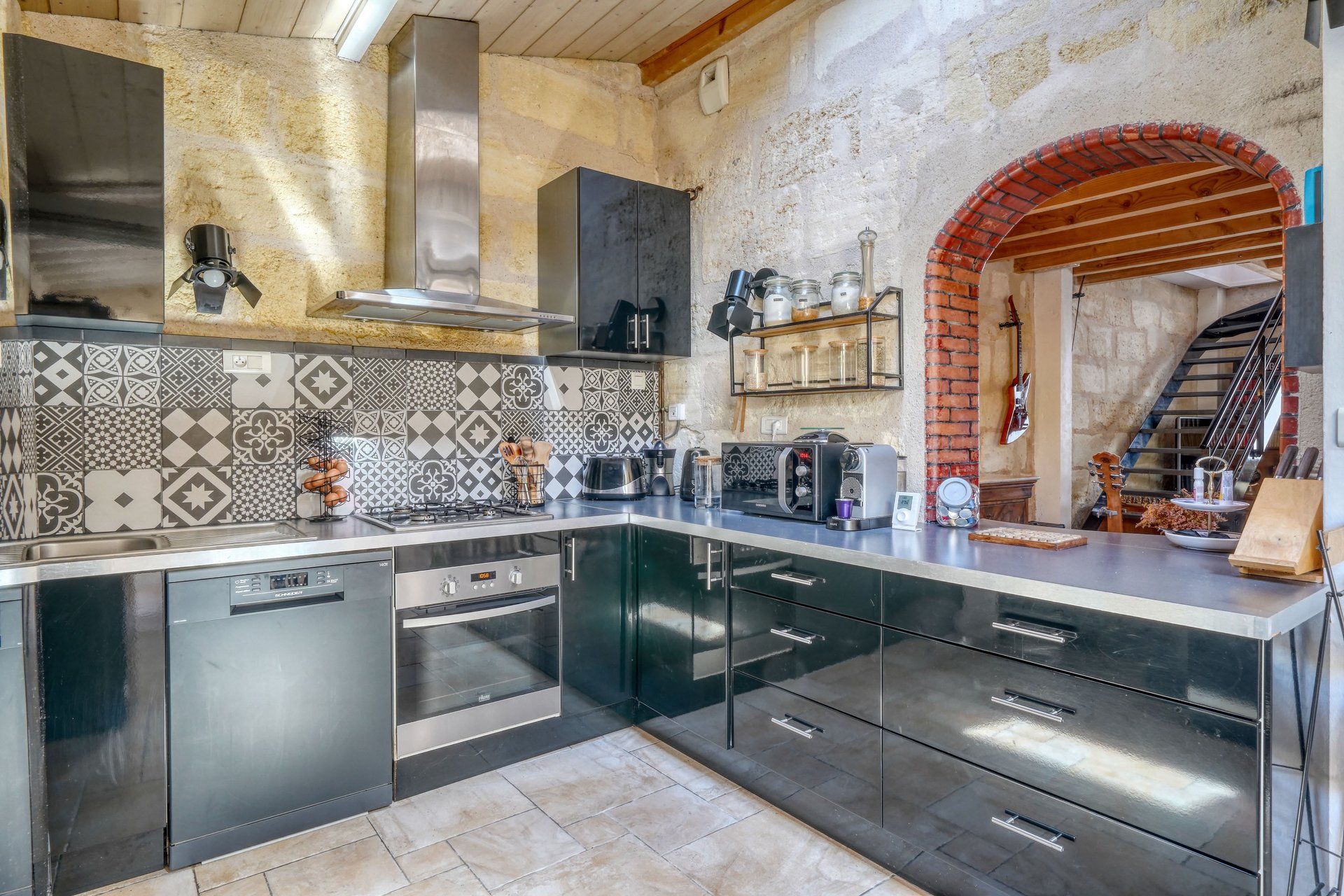 A modern kitchen with a large island, stainless steel appliances, and a unique exposed brick wall.