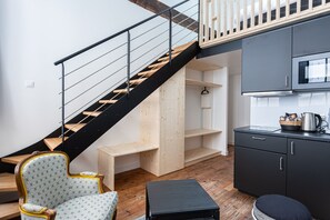 Ein modernes Interieur mit einer Holztreppe, einer Küchenzeile und einer Sitzecke mit einem gemusterten Sessel.