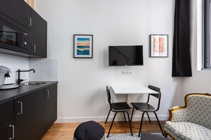 Ein kompakter Wohnbereich mit Küchenzeile, einem Essbereich mit zwei Stühlen, einem an der Wand befestigten Flachbildfernseher und einem Sofa.