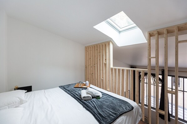 Ein Schlafzimmer mit Dachfenster, einem Bett mit weißen Leinen, einer dunklen Tagesdecke und einer Holzwand.