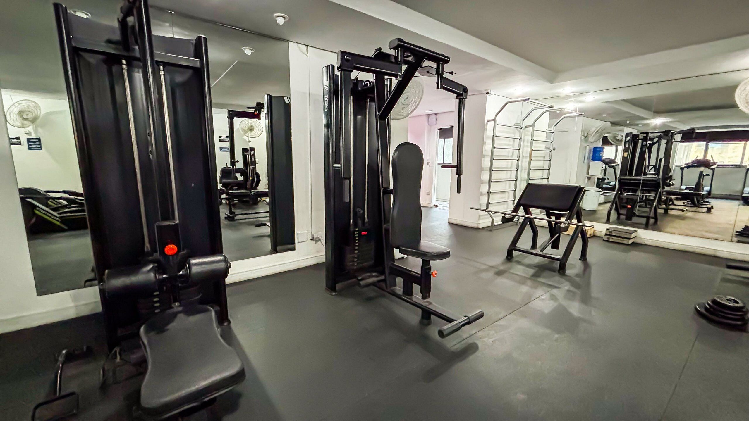 A gym with exercise equipment, mirrors, and a weight bench.