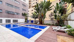 Ein Schwimmbecken mit zwei Bereichen, umgeben von einer Holzterrasse und verschiedenen tropischen Pflanzen.
