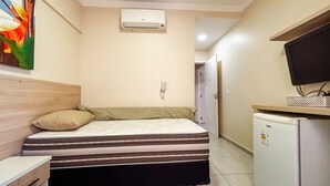 Ett litet hotellrum med en säng, ett skrivbord med en dator, en tv och en luftkonditioneringsanläggning.