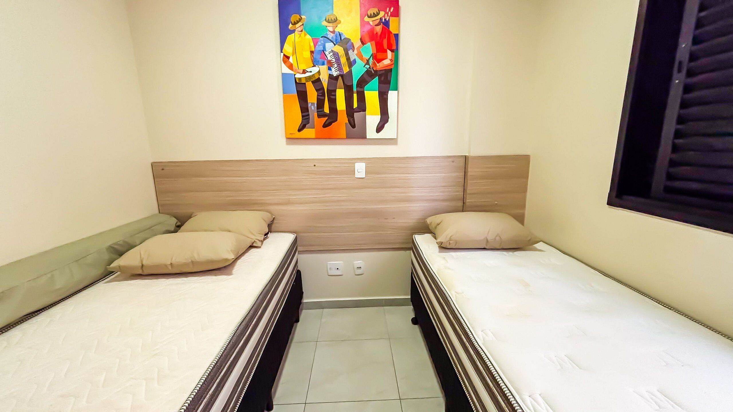 Quarto com duas camas, cabeceira de madeira, pintura colorida e janela com persianas.